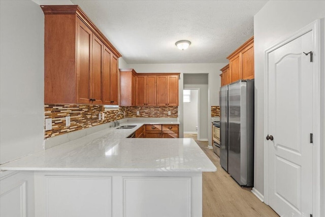 kitchen with backsplash, sink, light wood-type flooring, appliances with stainless steel finishes, and kitchen peninsula