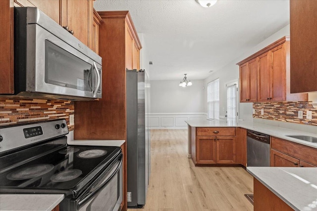 kitchen featuring backsplash, appliances with stainless steel finishes, decorative light fixtures, kitchen peninsula, and a chandelier