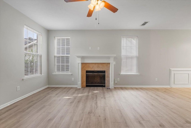 unfurnished living room featuring a tiled fireplace, ceiling fan, and light wood-type flooring