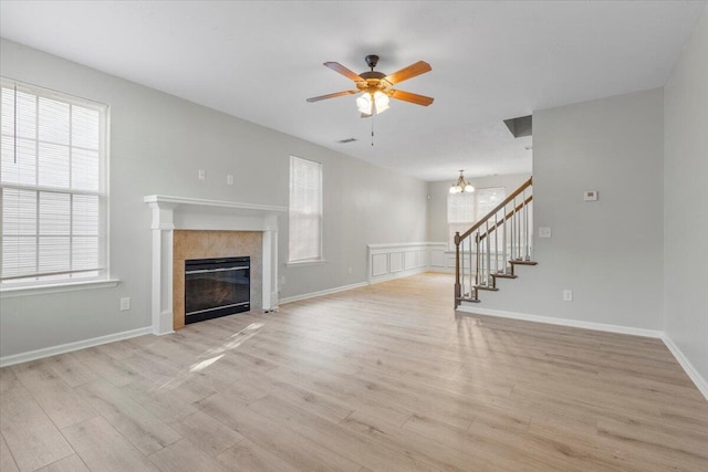 unfurnished living room with a tiled fireplace, ceiling fan with notable chandelier, and light hardwood / wood-style floors