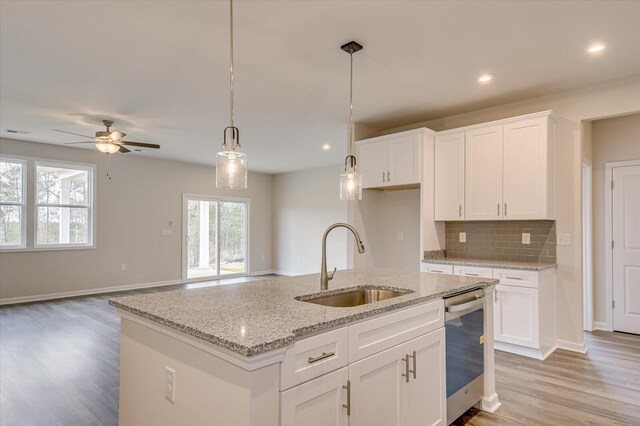 kitchen with white cabinetry, sink, light stone counters, stainless steel dishwasher, and a kitchen island with sink