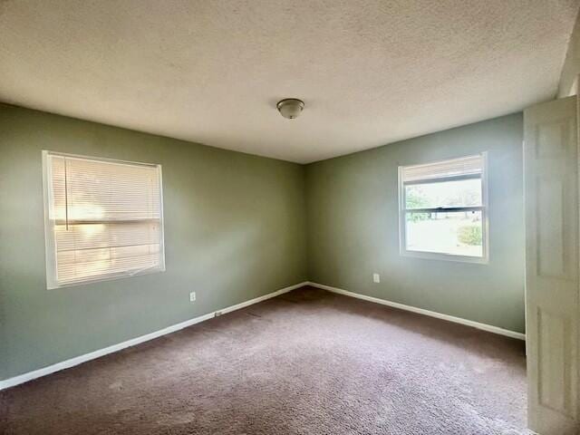 spare room with a textured ceiling, dark colored carpet, and baseboards