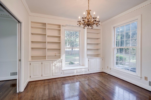 unfurnished dining area featuring an inviting chandelier, built in features, dark hardwood / wood-style floors, and ornamental molding