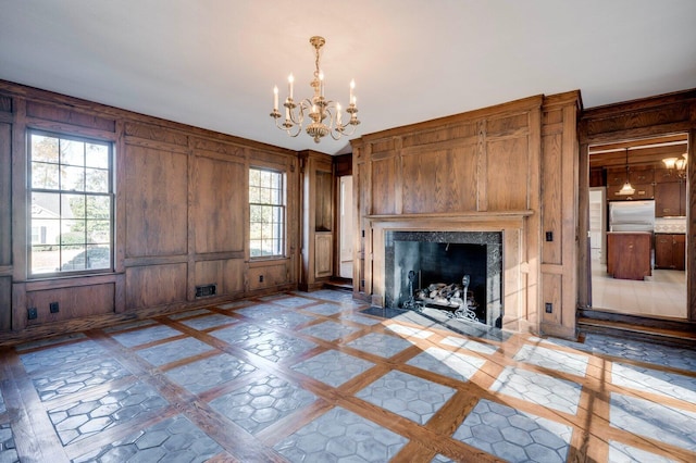 unfurnished living room featuring a chandelier, plenty of natural light, and wood walls