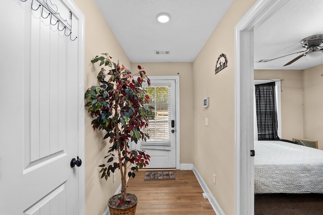 doorway with visible vents, a ceiling fan, baseboards, and wood finished floors