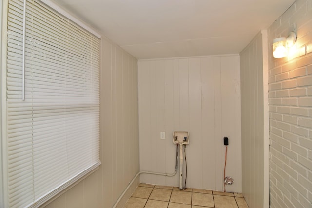 laundry area featuring wood walls, hookup for a washing machine, light tile patterned floors, and brick wall