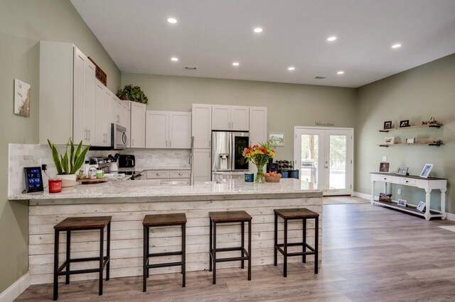 kitchen with white cabinetry, stainless steel appliances, backsplash, kitchen peninsula, and a kitchen bar