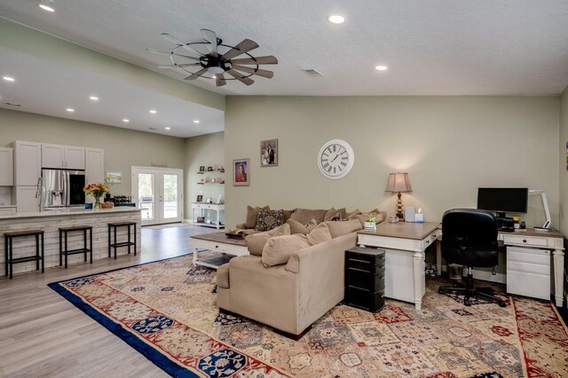 living room featuring french doors, light wood-type flooring, a textured ceiling, ceiling fan, and lofted ceiling