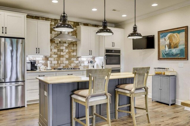 kitchen with white cabinets, a kitchen island, wall chimney range hood, and appliances with stainless steel finishes