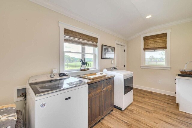 laundry room featuring washing machine and clothes dryer, a healthy amount of sunlight, light hardwood / wood-style flooring, and cabinets