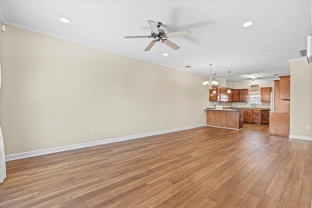 unfurnished living room with hardwood / wood-style floors, ceiling fan with notable chandelier, sink, and a textured ceiling