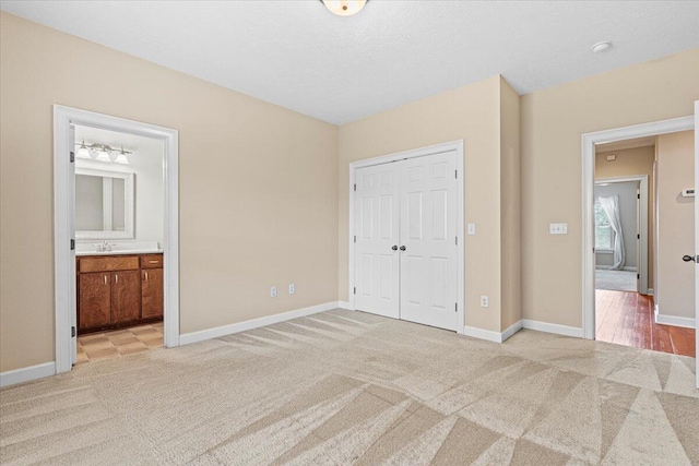 unfurnished bedroom with a closet, light carpet, and ensuite bath