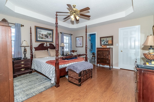 bedroom featuring a textured ceiling, a tray ceiling, wood finished floors, and baseboards