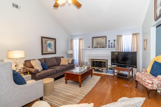 living area with visible vents, a fireplace with flush hearth, ceiling fan, wood finished floors, and high vaulted ceiling