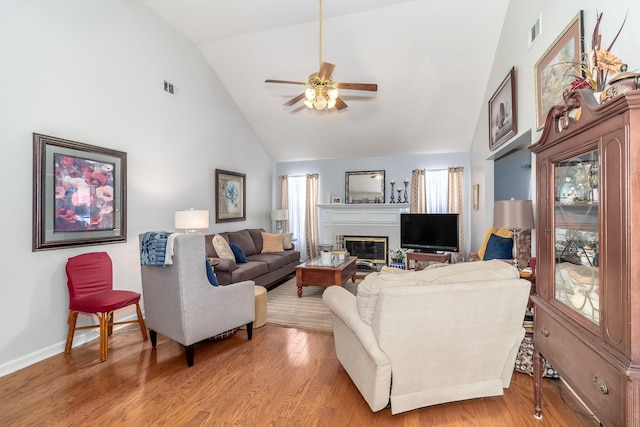 living room featuring high vaulted ceiling, a glass covered fireplace, visible vents, and wood finished floors