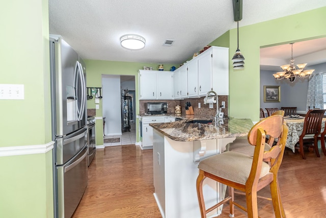 kitchen featuring stainless steel appliances, visible vents, white cabinetry, a sink, and a peninsula