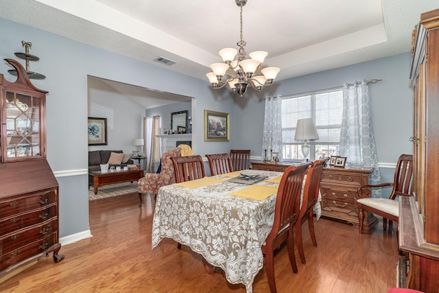 dining room featuring a raised ceiling, visible vents, light wood-style flooring, a chandelier, and baseboards