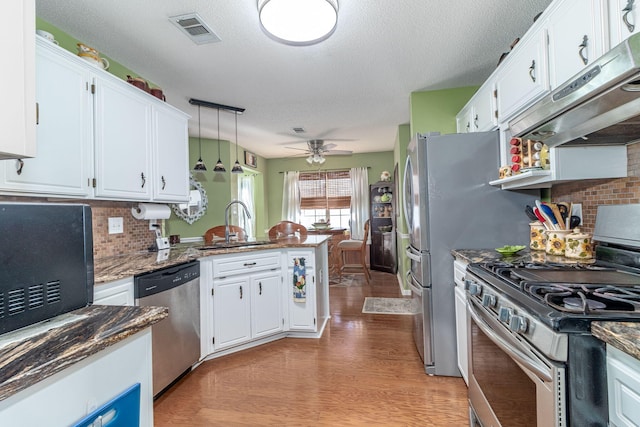 kitchen featuring visible vents, white cabinets, a peninsula, stainless steel appliances, and under cabinet range hood