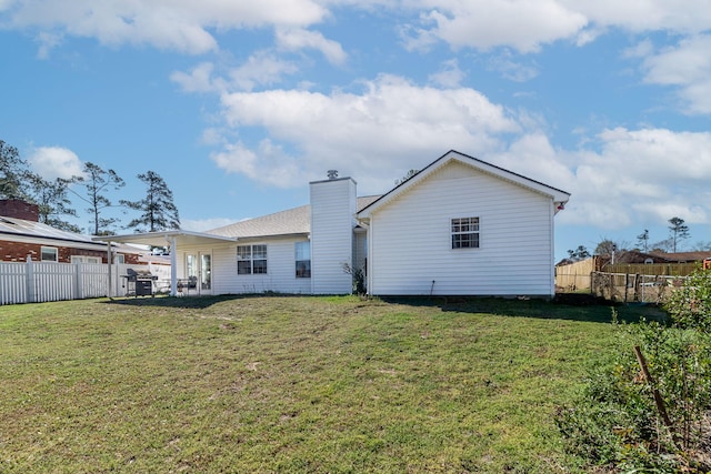 rear view of property with a lawn, a chimney, and fence