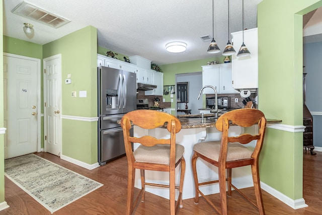 kitchen featuring appliances with stainless steel finishes, under cabinet range hood, visible vents, and a peninsula