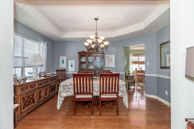 dining area featuring an inviting chandelier, baseboards, a raised ceiling, and wood finished floors