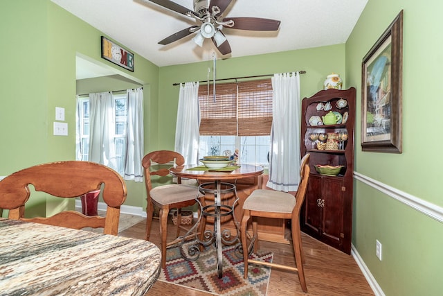 dining space featuring baseboards, wood finished floors, a ceiling fan, and a healthy amount of sunlight