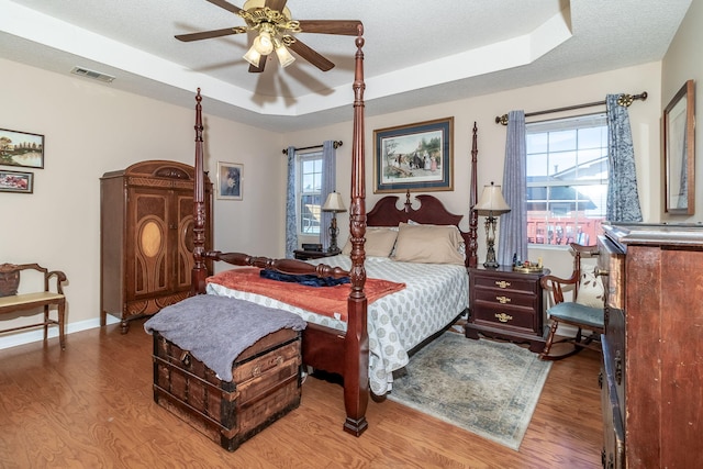 bedroom with a raised ceiling, a textured ceiling, and wood finished floors