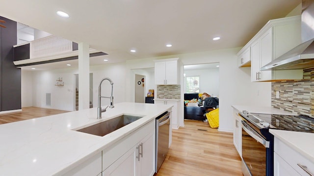 122 Ehrlich Farm Rd, Swainsboro, GA 30401 - kitchen featuring appliances with stainless steel finishes, wall chimney exhaust hood, white cabinetry, decorative backsplash, and light wood-type flooring