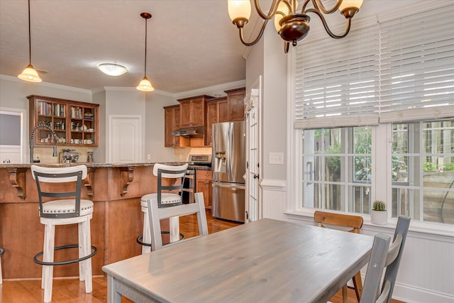 dining area featuring a chandelier, ornamental molding, a wainscoted wall, and light wood finished floors