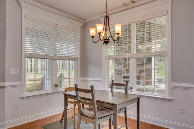 dining area with wainscoting, a chandelier, wood finished floors, and crown molding