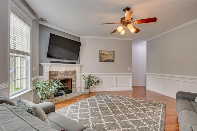 living area featuring ornamental molding, a ceiling fan, wood finished floors, a fireplace, and a wainscoted wall