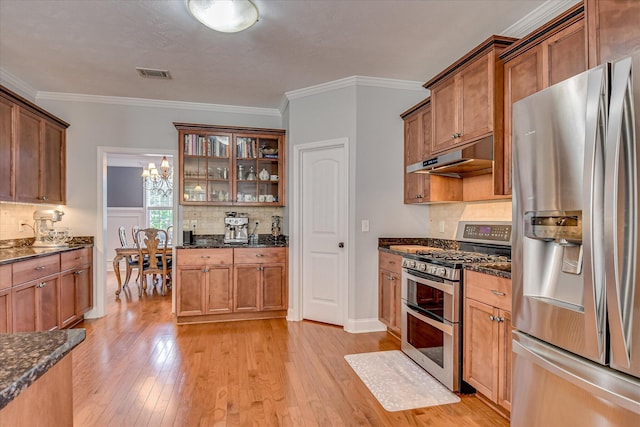 kitchen featuring stainless steel appliances, under cabinet range hood, backsplash, light wood-style floors, and glass insert cabinets