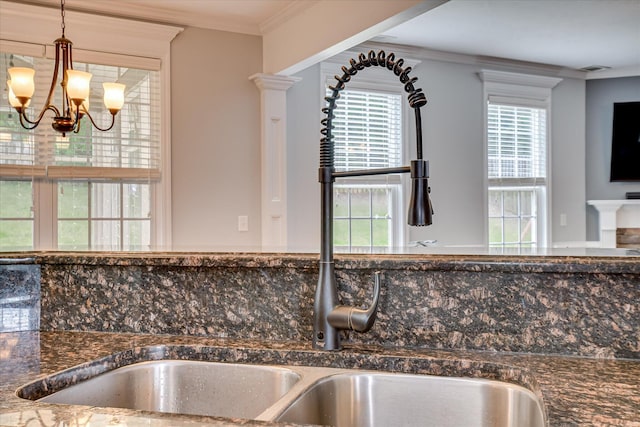 detailed view of a chandelier, crown molding, a sink, hanging light fixtures, and dark stone counters