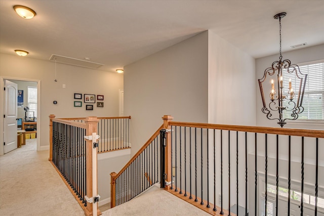corridor featuring attic access, an upstairs landing, carpet floors, and a chandelier