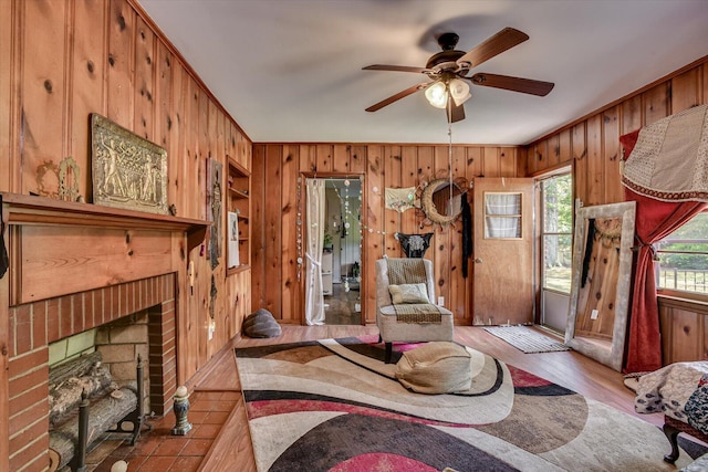 living room featuring wooden walls, ceiling fan, ornamental molding, a fireplace, and light hardwood / wood-style floors