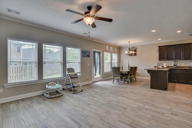 interior space featuring pendant lighting, a center island with sink, ceiling fan with notable chandelier, crown molding, and dark brown cabinets