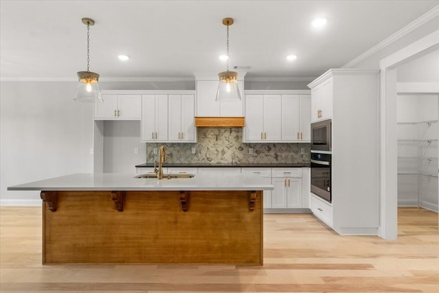 kitchen featuring sink, stainless steel microwave, oven, a kitchen island with sink, and white cabinets