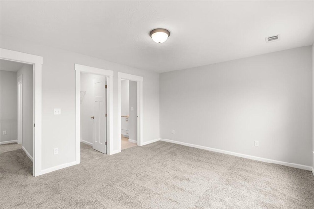 unfurnished bedroom with light carpet, a spacious closet, and ensuite bath