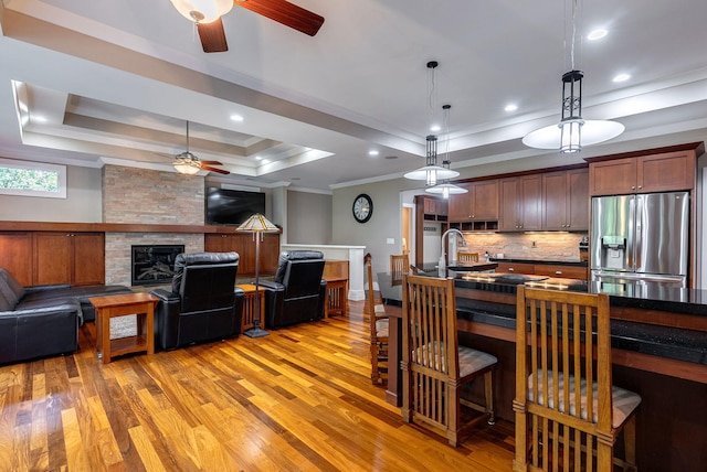 kitchen featuring a large fireplace, hanging light fixtures, a raised ceiling, stainless steel fridge, and decorative backsplash