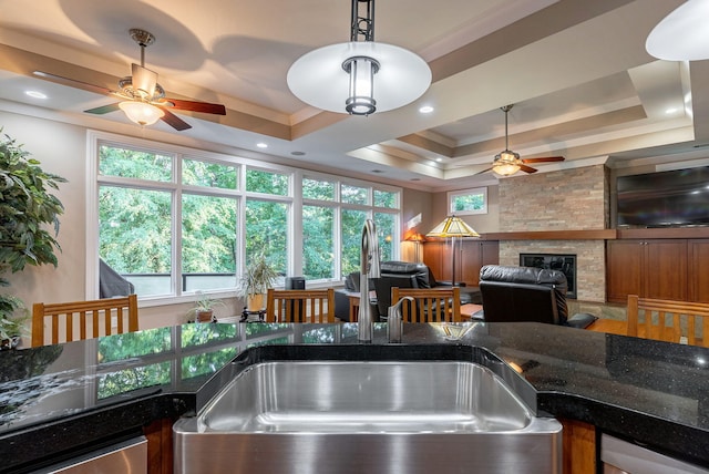 kitchen with pendant lighting, a raised ceiling, sink, crown molding, and a fireplace