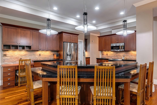 kitchen featuring decorative backsplash, appliances with stainless steel finishes, crown molding, decorative light fixtures, and hardwood / wood-style floors