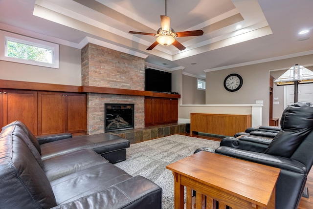 living room featuring a stone fireplace, crown molding, hardwood / wood-style flooring, ceiling fan, and a tray ceiling