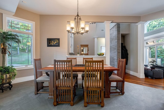 dining space with wood-type flooring, decorative columns, a wealth of natural light, and an inviting chandelier