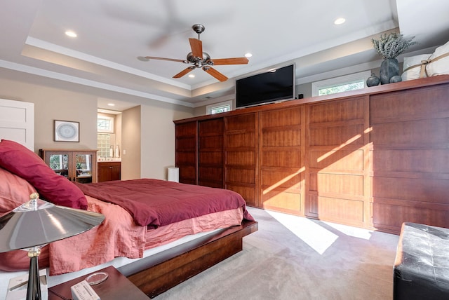 carpeted bedroom with a tray ceiling, multiple windows, and ceiling fan