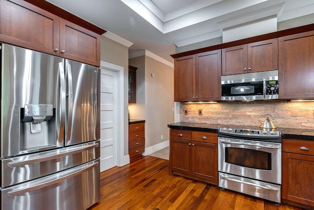 kitchen with backsplash, dark wood-type flooring, dark stone countertops, ornamental molding, and stainless steel appliances