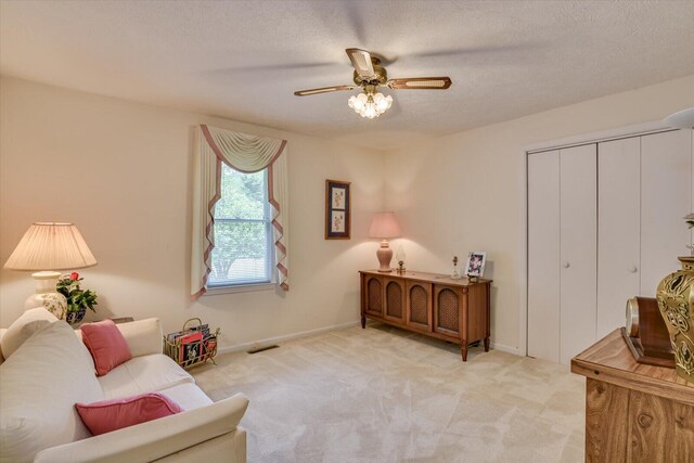 living area with a textured ceiling, light colored carpet, and ceiling fan