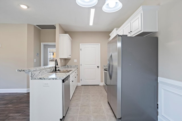 kitchen featuring appliances with stainless steel finishes, sink, white cabinets, kitchen peninsula, and light stone countertops