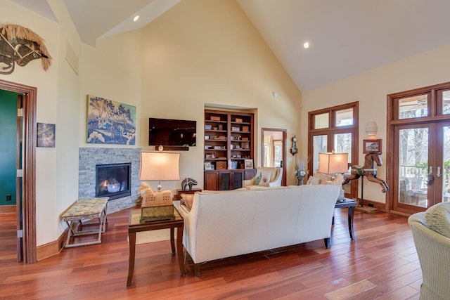 living room with french doors, built in shelves, wood-type flooring, high vaulted ceiling, and a stone fireplace