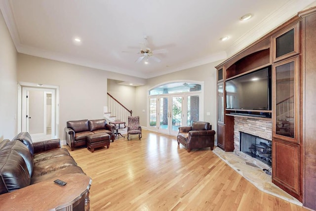 living room with a stone fireplace, french doors, ornamental molding, and light wood-type flooring