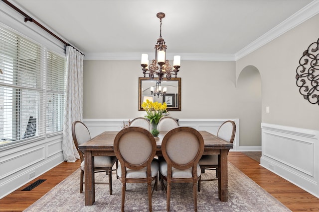 dining room with crown molding, arched walkways, wood finished floors, and a chandelier